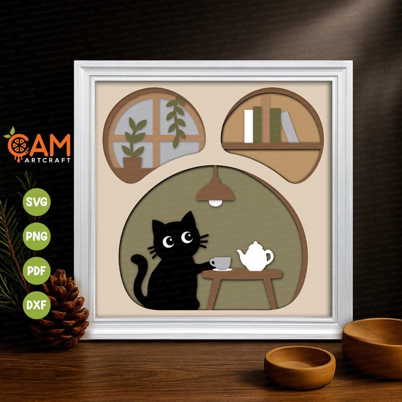 May include: A layered paper art piece in a white frame featuring a black cat sitting at a small table with a white teapot and cup. Above the cat, a circular window with a plant and a shelf with books are depicted in a cutout style on a beige background.