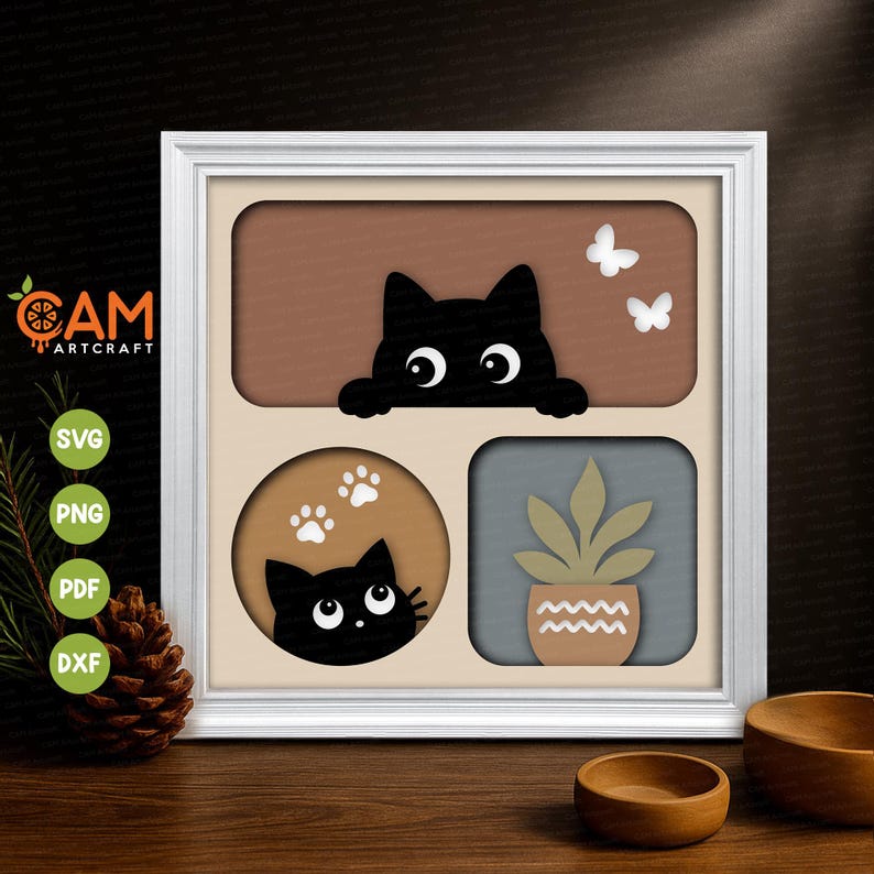 May include: A white square frame containing a layered paper art piece. The top section shows a black cat peeking over a brown rectangle with two white butterflies. The bottom left circle features a black cat and white paw prints. A potted plant is on the right.