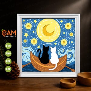 Op de afbeelding: Een ingelijst papieren kunstwerk met een zwart-wit kattenpaar in een boot onder een sterrenhemel met een halve maan. Het kunstwerk zit in een witte lijst en bevat de tekst "CAM Artcraft".