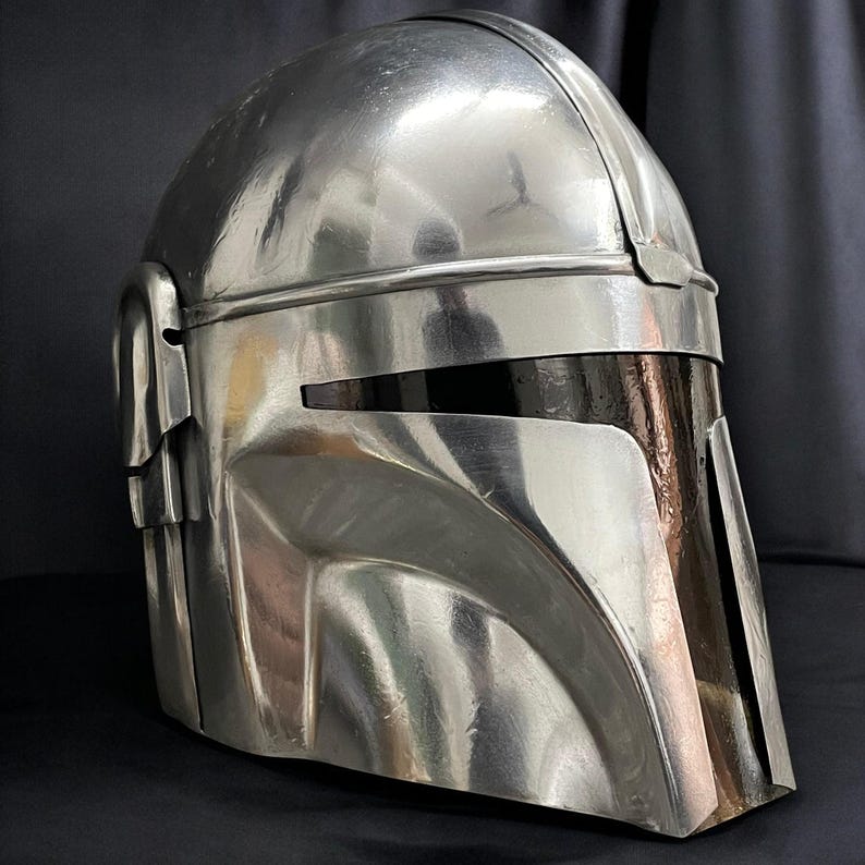 May include: A metallic silver helmet with a visor, likely a prop or collectible. The helmet has a smooth, reflective surface with visible seams and details. The design suggests a futuristic or science fiction theme.