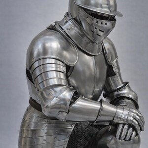 May include: A full suit of polished steel armor, including a helmet with a visor, shoulder and arm protection, and leg and knee guards. The medieval armor is shown in a kneeling position, with the hands resting on the knees.