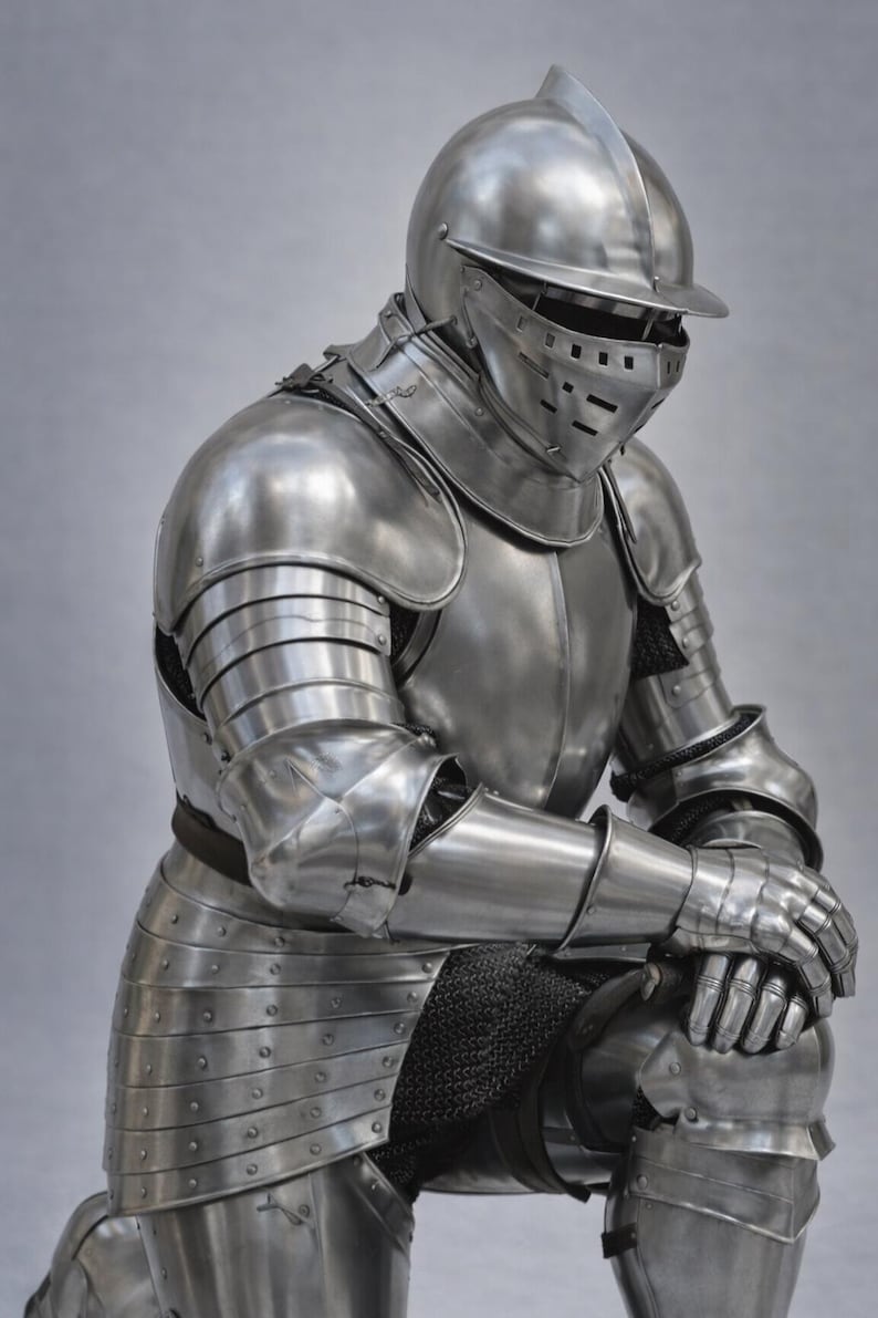 May include: A full suit of polished steel armor, including a helmet with a visor, shoulder and arm protection, and leg and knee guards. The medieval armor is shown in a kneeling position, with the hands resting on the knees.