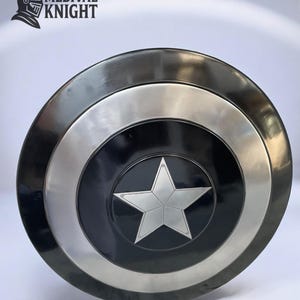 May include: A round, metallic shield with a black center featuring a silver star. The shield has a silver ring and a dark gray outer rim. The text "MEDIVAL KNIGHT" and a knight's helmet logo are in the upper left corner.