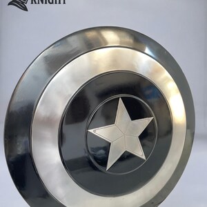May include: A round, metallic shield with a central star design. The shield features concentric circles in black, silver, and a darker metallic tone. The shield has the text "MEDIVAL KNIGHT" and a knight's helmet logo.