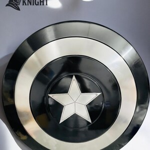 May include: A black and silver shield with a white star in the center. The shield has concentric rings of black, silver, and black. The logo "MEDIVAL KNIGHT" is in the upper left corner.