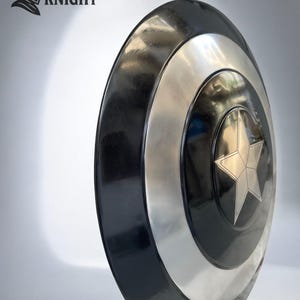 May include: A round shield with a black outer ring, a silver band, and a central black circle with a silver star. The shield has a glossy finish. The text "MEDIVAL KNIGHT" and a knight's helmet logo are in the upper left corner.