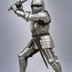 May include: A full suit of polished steel medieval armor, including a helmet, chest plate, and leg guards. The knight is holding a longsword aloft with both hands. The image includes the text "MEDIVAL KNIGHT" in the upper left corner.