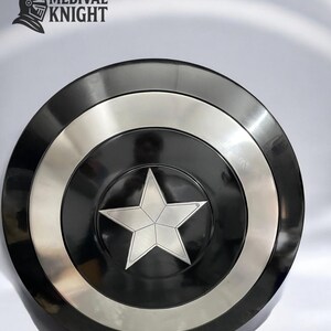 May include: A black and silver shield with a central silver star design. The shield has a circular shape with a black center, a silver ring, and a black outer rim. The text "MEDIVAL KNIGHT" is in the upper left corner.