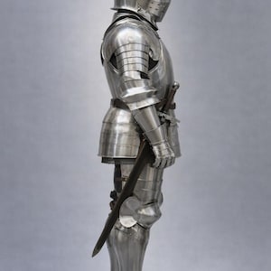 May include: A full suit of polished steel armor, including a helmet, chest plate, arm and leg protection, and gauntlets. A sword is attached to the side. The image includes the text "MEDIEVAL KNIGHT" in the upper left corner.