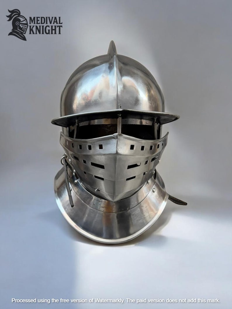 May include: A polished, silver-colored medieval knight's helmet. The helmet features a visor with horizontal slits for vision and ventilation, a pointed top, and a neck guard. The logo "MEDIVAL KNIGHT" is visible in the upper left corner.