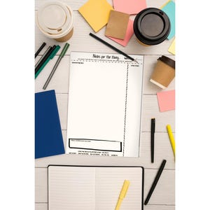 May include: An overhead shot of a workspace with a notepad that reads "Notes for the thing." The scene includes coffee cups, pens, sticky notes, and a blue notebook. The notepad is open, and the pens are black, green, and yellow.