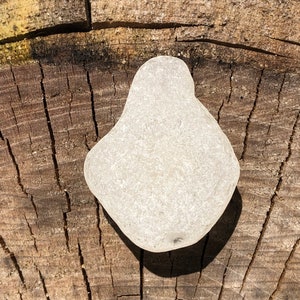 May include: A smooth, white, sea glass piece with an irregular shape, resting on a weathered wooden surface.