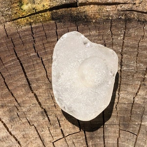 May include: A smooth, white sea glass piece with a slightly cloudy appearance, resting on a weathered wooden surface.