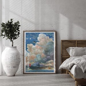May include: A framed poster featuring a vibrant illustration of a fantastical scene with a flying creature soaring through clouds. The poster has Japanese text and is displayed in a bedroom setting with a plant in a large white vase.