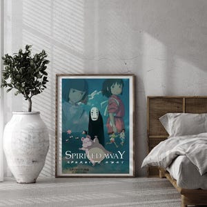 May include: A framed poster featuring artwork from the animated film "Spirited Away." The poster has a wooden frame and is displayed in a room with a neutral color scheme. The artwork depicts characters from the film in a vibrant, colorful style.