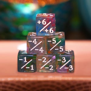 Puede incluir: Una pila de seis dados translúcidos de colores con números blancos y líneas diagonales. Los dados están dispuestos en forma de pirámide, con el dado superior mostrando +6. Los dados tienen un aspecto veteado con tonos de azul, rojo, verde y morado.
