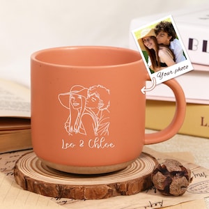 Könnte beinhalten: Terrakottafarbene Keramiktasse mit einer weißen Strichzeichnung eines Paares und den Namen "Leo & Chloe". Ein kleines Foto mit den Worten "Your photo" ist angebracht. Die Tasse steht auf einem Holzuntersetzer.