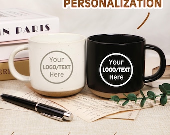 May include: Two ceramic mugs, one white and one black, with a customizable logo area. The mugs have a speckled finish and a natural-colored base. A black pen rests in front of the mugs. Text on the image reads "PERSONALIZATION".