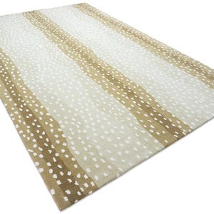 May include: A rectangular area rug featuring a repeating pattern of vertical stripes in shades of tan and beige. The design is overlaid with a consistent pattern of small, white, elongated oval spots that create a textured, dappled appearance.