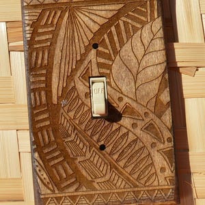 May include: Wooden light switch cover with intricate carved designs. The cover features a central switch labeled "OFF" and is set against a woven bamboo background. The carved patterns include geometric shapes and leaf-like motifs.