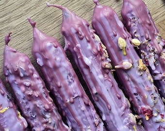 May include: A set of five tapered candles in a deep lavender hue, featuring a textured, dripped wax finish. Each candle is embedded with dried flower petals and small botanical elements, creating a layered, rustic appearance across the surface.