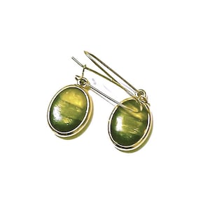 May include: A pair of gold-colored earrings with oval-shaped, green-hued stones. The stones have a marbled appearance, and the earrings are set in a gold-tone metal. The earrings are designed with a hook closure.