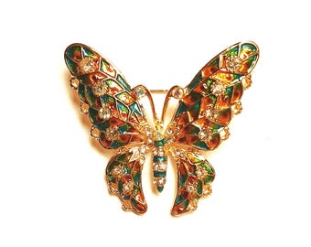 May include: A gold butterfly brooch with detailed enamel work in green, orange, and brown. The wings are embellished with clear crystals. The body has a striped design, and the brooch has a pin fastening for secure wear.