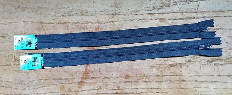 May include: Two blue denim zippers with silver metal pulls and the brand name "Ziplon" printed on the packaging. One zipper is 12 inches long, and the other is 17 inches long. The zippers are laid out on a wooden surface.