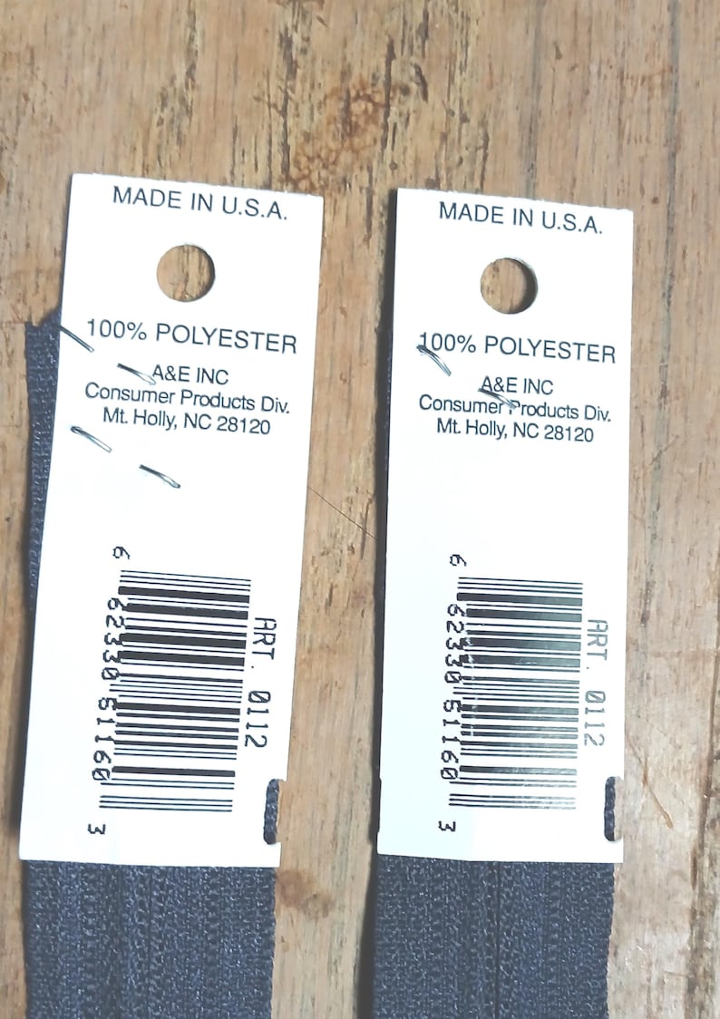 May include: Two dark gray zippers with white tags. The tags read "MADE IN U.S.A." and include the text "100% POLYESTER" and the manufacturer's information. Each tag has a barcode and the text "ART. 0112".