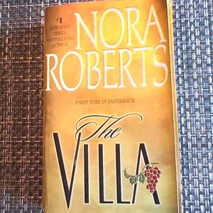 May include: A paperback book titled "The Villa" by Nora Roberts. The cover is a gradient of yellow and gold with the title in large black letters. The cover also includes a cluster of grapes.