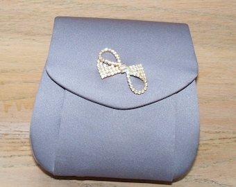 May include: A gray satin clutch purse with a rhinestone bow embellishment.