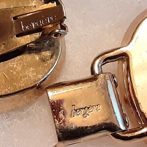 以下が含まれることがあります： ブランド名「bergere」が刻印されたクリップ式メカニズムと留め具を備えたゴールドトーンの金属製ジュエリー。金属表面は光沢のある仕上げで、金属の質感や構造部品がはっきりと確認できます。