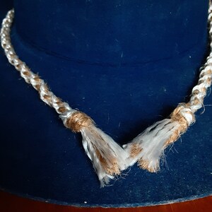 Puede incluir: Un collar de cuerda blanco y marr&oacute;n con borlas sobre un fondo azul.