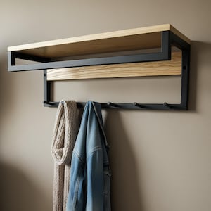 May include: A wall-mounted coat rack with a light wood shelf and a black metal frame. Below the shelf are hooks for coats and accessories. A denim jacket and a beige scarf hang from the hooks.