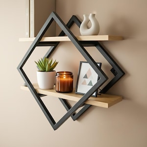 Op de afbeelding: Een moderne wandplank met een geometrisch zwart metalen frame en twee lichte houten planken. De planken tonen een kleine potplant, een kaars in een glazen pot, een fotolijst, een decoratieve vaas en twee boeken.