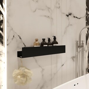 May include: A contemporary bathroom setup with a black shelf displaying brown bottles with pumps and a clear bottle. A beige loofah hangs beneath. The backdrop is a white marble wall with black veining, and a silver tap.