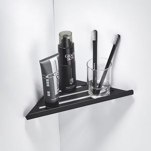 May include: A black, triangular corner shelf holds toiletries. Items include a tube of "CHILDES" moisturizing cream, a "GRACE SON" bottle, two black toothbrushes in a glass, and a black shelf. The shelf is mounted on a white wall.