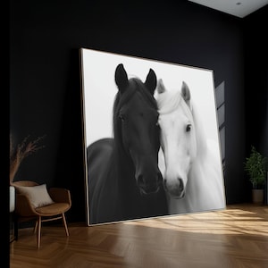 Könnte beinhalten: Schwarz-Weiß-Kunstdruck mit zwei Pferden, einem schwarzen und einem weißen, die ihre Köpfe aneinanderlegen. Das Kunstwerk wird in einem Raum mit schwarzer Wand, Holzboden und Stuhl ausgestellt.
