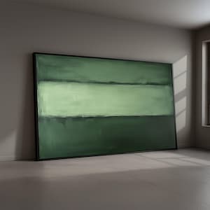 May include: Large abstract painting in a black frame. The artwork features a horizontal composition with shades of green, including a lighter central band. The painting leans against a wall in a room with natural light.