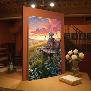 Puede incluir: Una impresión artística enmarcada representa un esqueleto sentado en un banco de madera, con vistas a un paisaje vibrante. La obra de arte presenta una colorida puesta de sol, colinas y flores silvestres. Un pájaro vuela en la distancia. La impresión se exhibe sobre una mesa.