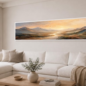 Op de afbeelding: Een panoramisch landschapsschilderij in een witte lijst met een gouden zonsondergang boven een bergketen en een kronkelende rivier. Het kunstwerk toont warme oranje en gele tinten in de lucht, contrasterend met diepblauwe en bruine tinten in het terrein.