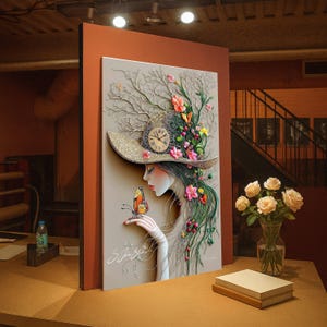 Puede incluir: Una obra de arte enmarcada que representa a una mujer con pelo largo verde, un sombrero floral y una mariposa. La obra de arte tiene un fondo neutro y está decorada con flores y un reloj. La obra de arte se exhibe sobre una mesa de madera.