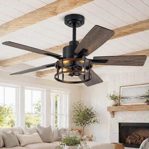 May include: A black and brown ceiling fan with five wooden blades. The fan has a black motor housing and a decorative cage around the light fixtures. The blades have a wood grain finish. The fan is installed in a living room with a white ceiling and exposed wooden beams.