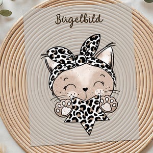 Könnte beinhalten: Eine skurrile Illustration einer Katze mit Leoparden-Stirnband und Stern. Die Katze lächelt mit geschlossenen Augen. Das Bild befindet sich auf einem beigen Hintergrund mit dem Wort "Bügelbild" oben.