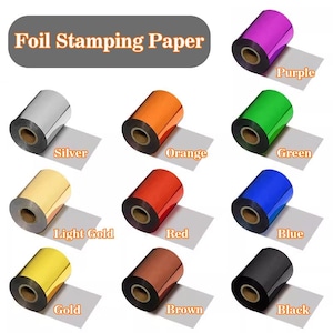 Puede incluir: Una colección de rollos de papel de estampado en caliente en varios colores: plata, naranja, morado, verde, rojo, azul, dorado, oro claro, marrón y negro. El texto "Foil Stamping Paper" está en la parte superior.