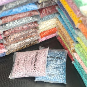 May include: Bags of colorful sealing wax particles in various shades, including pink, blue, yellow, and orange. The bags are transparent, allowing the wax colors to be visible. The text "SEALING WAX PARTICLES" is printed on the bags.