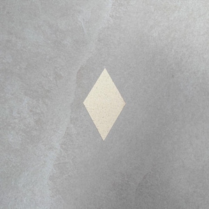 Könnte beinhalten: Ein rautenförmiges, cremefarbenes Objekt mit gesprenkelter Textur ist vor einem marmorierten grauen Hintergrund zentriert. Die Rautenform hat eine neutrale Farbe und kontrastiert mit dem grauen Hintergrund.
