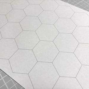 Könnte beinhalten: Ein Blatt weißes Papier mit einem sich wiederholenden Muster aus grauen sechseckigen Formen. Die Sechsecke sind mit dünnen grauen Linien umrandet. Das Papier liegt auf einer grauen Schneidematte.