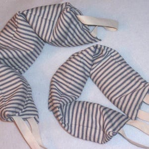 May include: Two striped fabric neck wraps with cream-colored straps. The fabric has a cream background with navy blue vertical stripes. The wraps are curved and appear to be filled with a soft material.