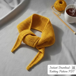 Puede incluir: Bufanda de punto de color amarillo mostaza con un patrón texturizado. La bufanda está anudada, con los extremos colgando. Una madeja de lana, agujas de tejer y una taza de té están en el fondo. El texto de la imagen dice "Instant Download - Knitting Pattern PDF."